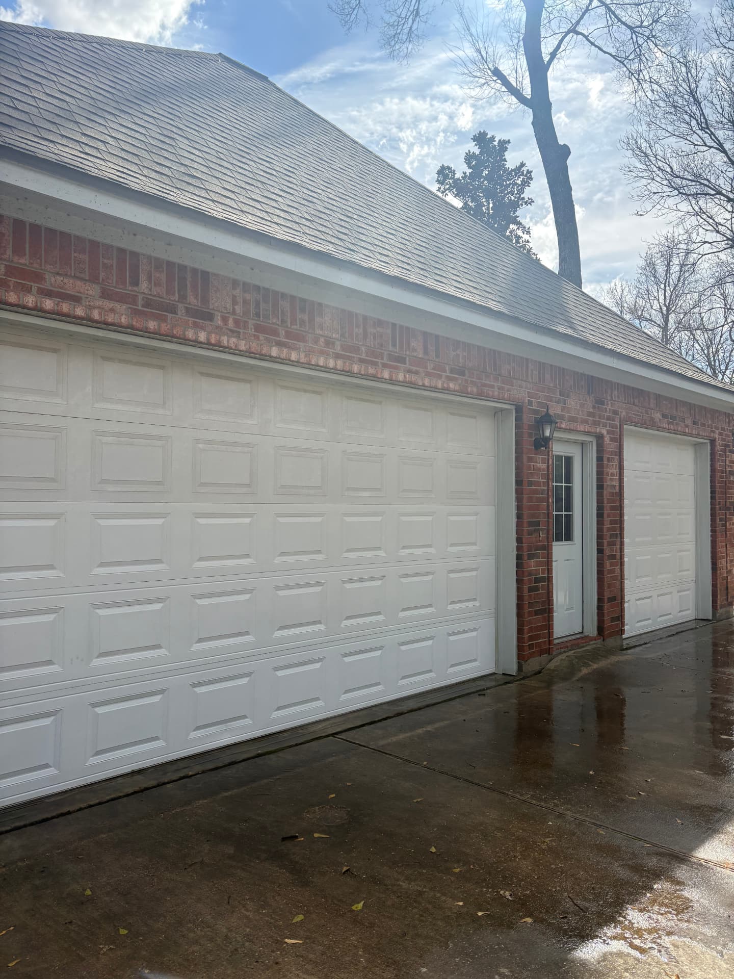 Brick home with white garage doors and a freshly washed wet driveway — pressure washing in Montgomery, TX