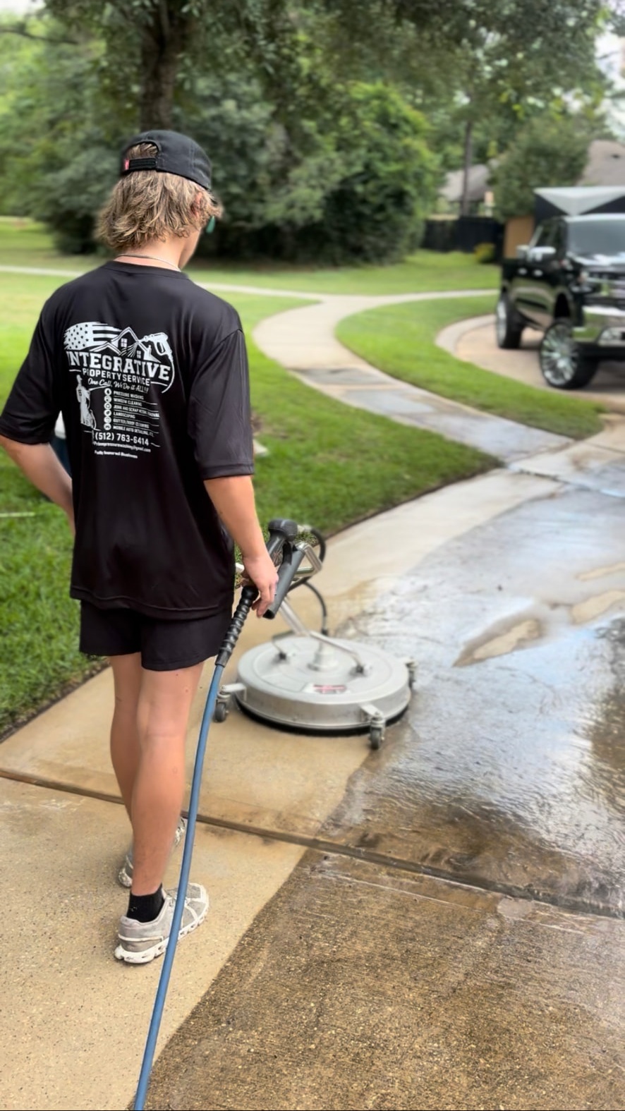 Integrative team member pressure washing a concrete driveway with a surface cleaner — Integrative Services, Montgomery TX